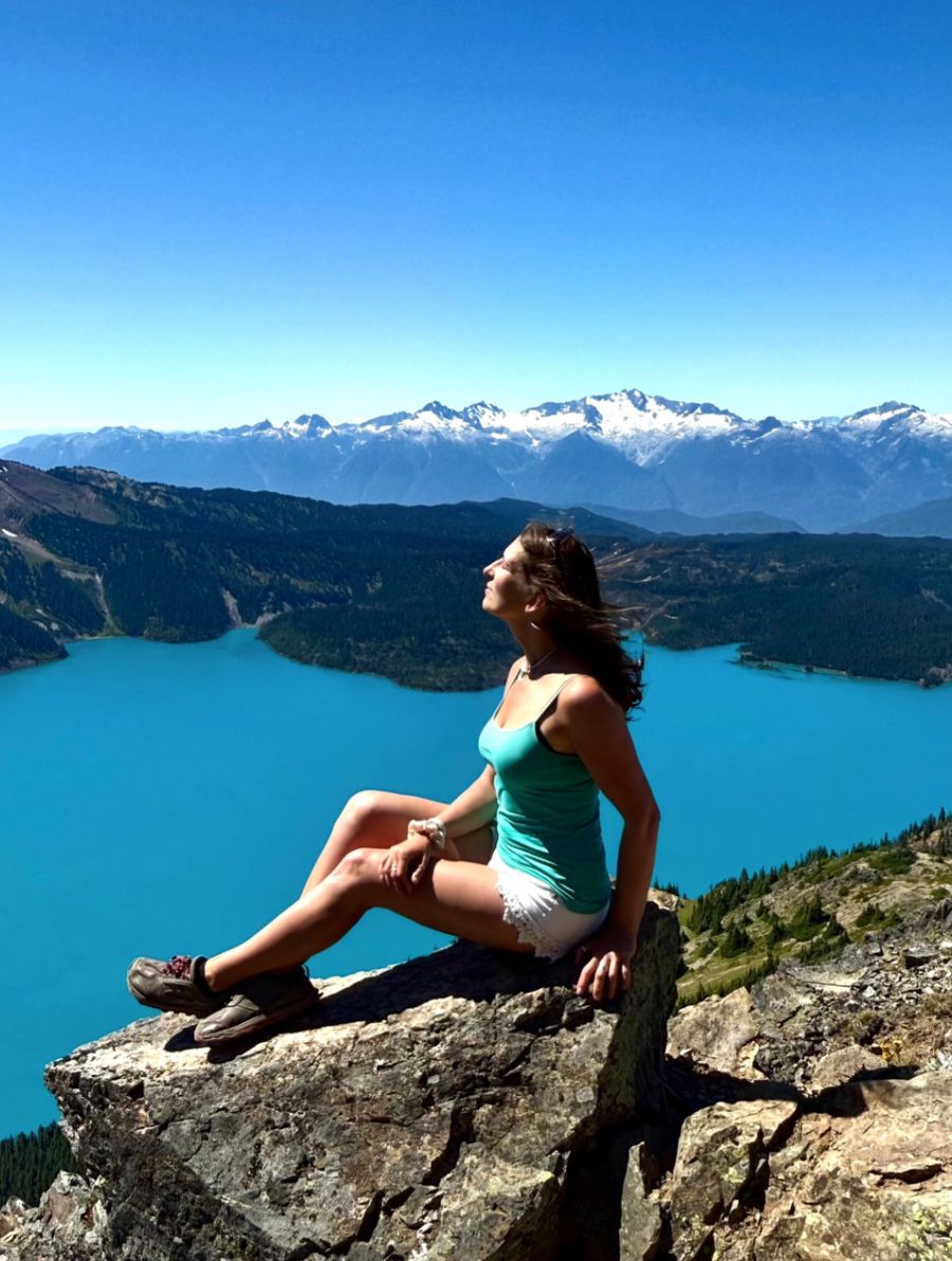 Monika resting on a rock above a turquoise alpine lake